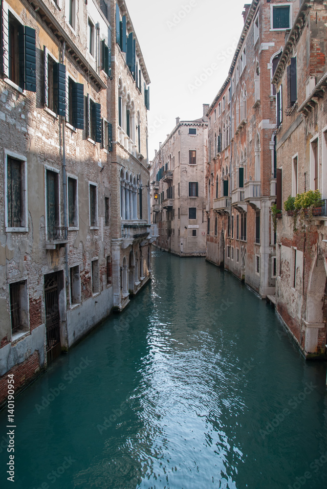Narrow water canal, ancient buildings with rustic brick facades, Venice, Italy