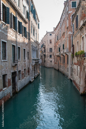 Narrow water canal, ancient buildings with rustic brick facades, Venice, Italy © Neeqolah
