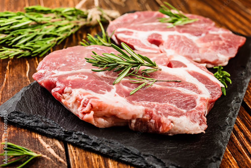 Raw pork steaks with seasonings on a wooden surface Raw pork steaks with seasonings on a wooden surface