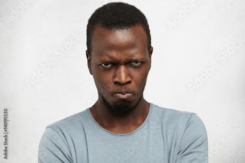 Studio portrait of displeased, angry, grumpy and pissed off young African American male looking and frowning at camera, pursing lips, having bad mood, feeling dissatisfied and furious with something