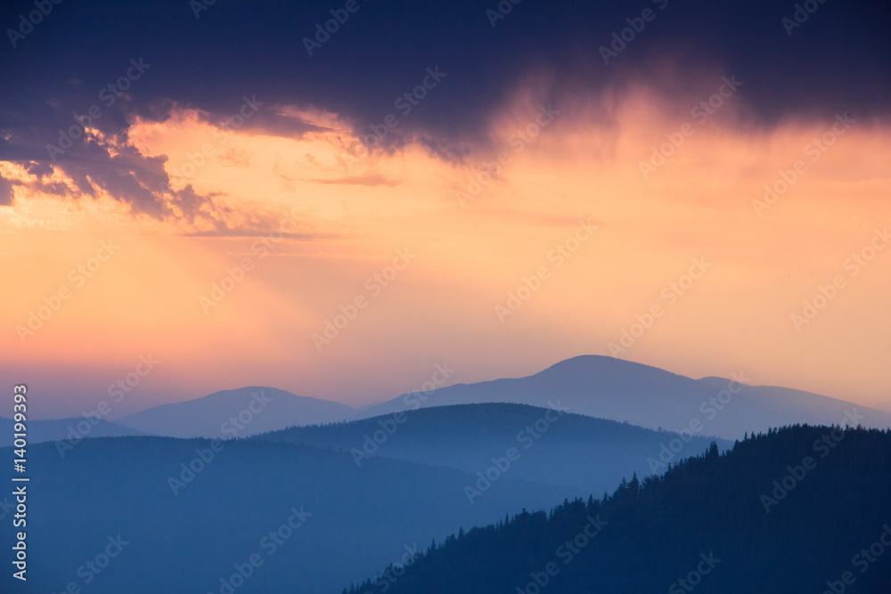 Fantastic sunrise above peaks of smoky mountain with the view into misty hills. Dramatic overcast sky. Mountains silhouettes.