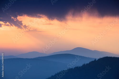 Fantastic sunrise above peaks of smoky mountain with the view into misty hills. Dramatic overcast sky. Mountains silhouettes.