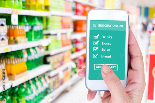 Hand holding smart phone with grocery shopping check list online on screen device over blur product shelves in supermarket background, business and technology, digital marketing concept