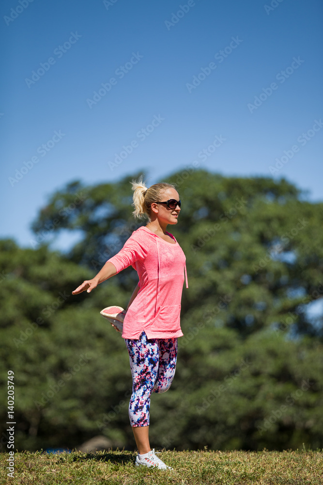 Young sportive woman stretching in the sunny park, outdoors. Working out outside. Healthy lifestyle. Doing exercises. Blue sky background.