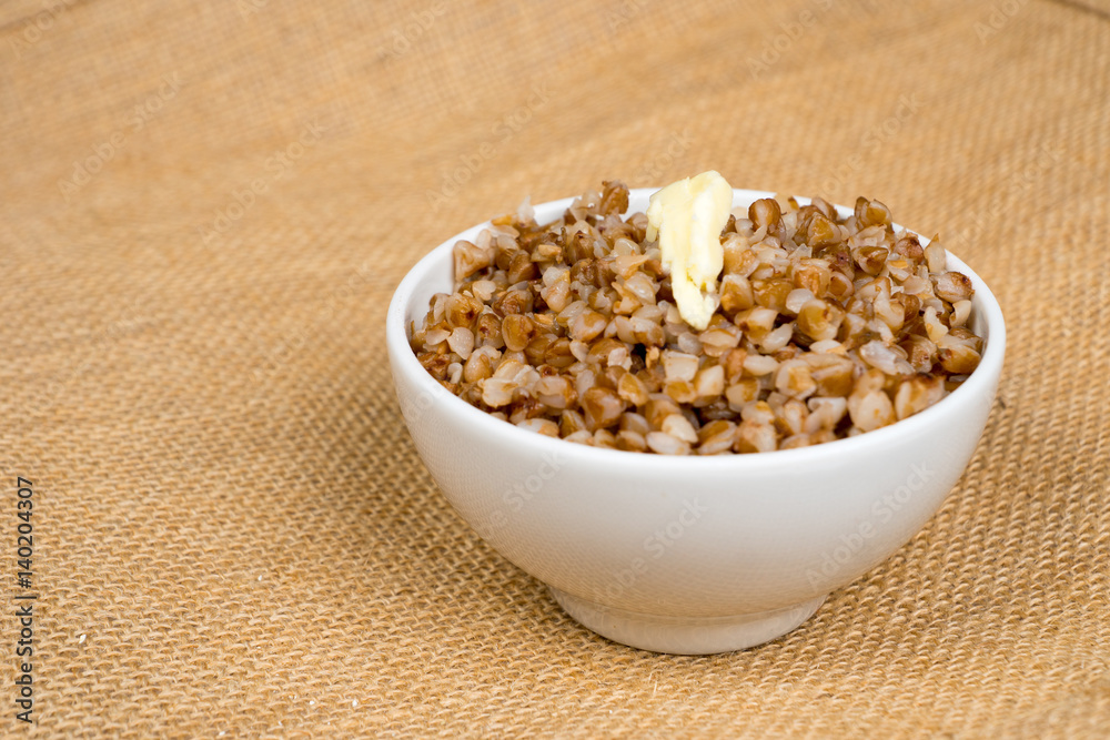 cooked buckwheat heap with butter in white bowl over sackcloth cooked buckwheat heap with butter in white bowl over sackcloth