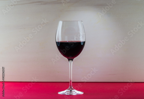 Polished still life glass of wine with nice light effect in red and beige background