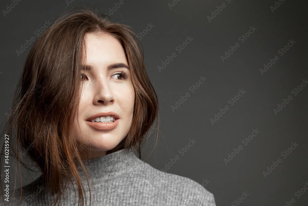 Close-up portrait of smiling happy cute brunette girl with clear skin on gray background