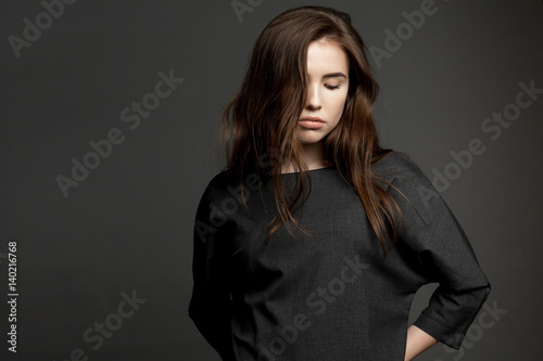 Young cute brunette model woman in dark dress on gray background.