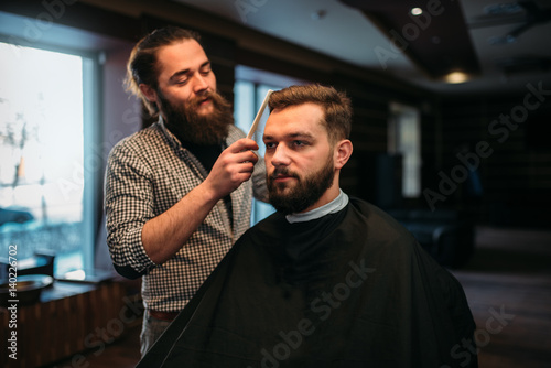 Barber combing hair of the client in salon cape photo