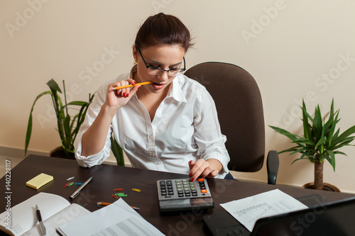 Young female bookkeeper considers on calculator photo