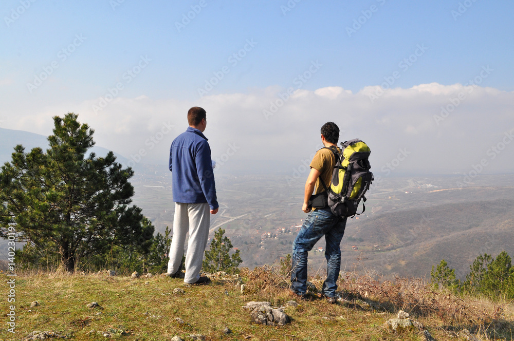 Two hikers standing on top of the hill over the city and looking down