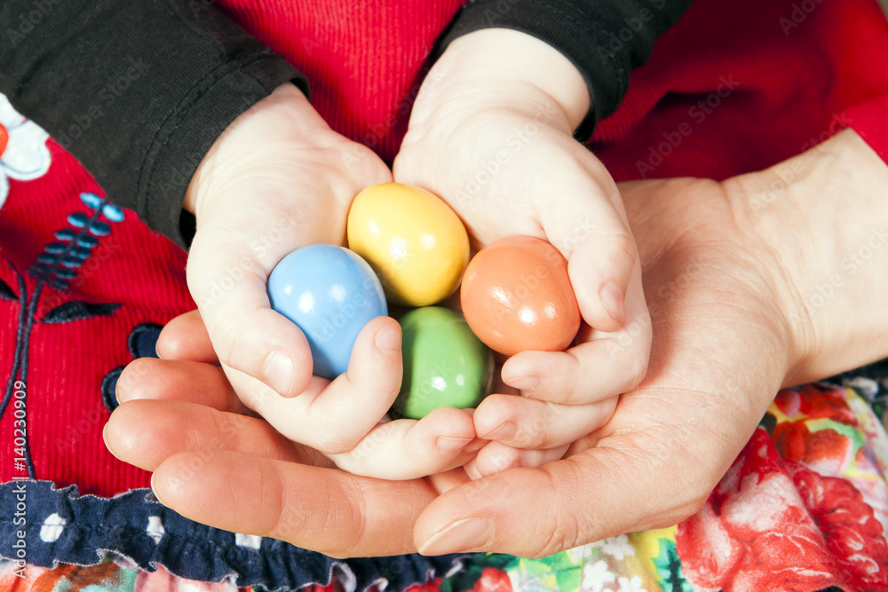 Little girl holding Easter eggs in her and mother’s hands. Colorful background. Little girl holding Easter eggs in her and mother’s hands. Colorful background.