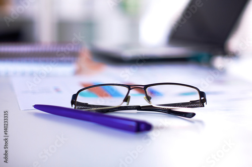 Glasses and pen in focus lie on the table