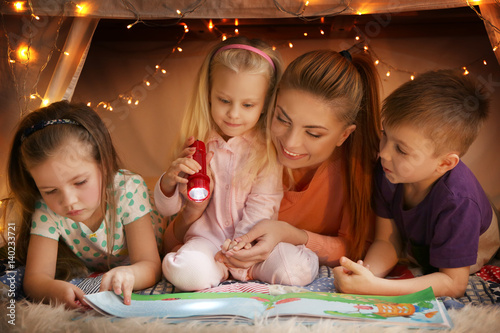 Slika na platnu Young woman and cute children reading book in hovel at home