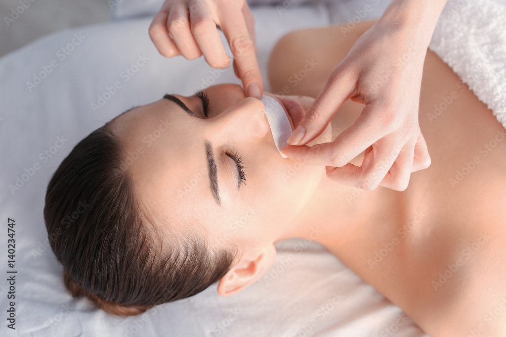 Beautician depilating young woman's face with wax in spa center Beautician depilating young woman's face with wax in spa center