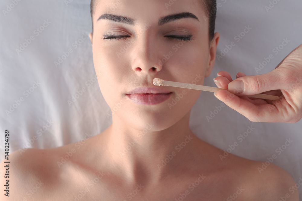 Beautician depilating young woman's face with wax in spa center Beautician depilating young woman's face with wax in spa center