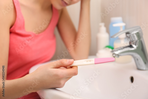 Young woman with pregnancy test near sink in bathroom, closeup