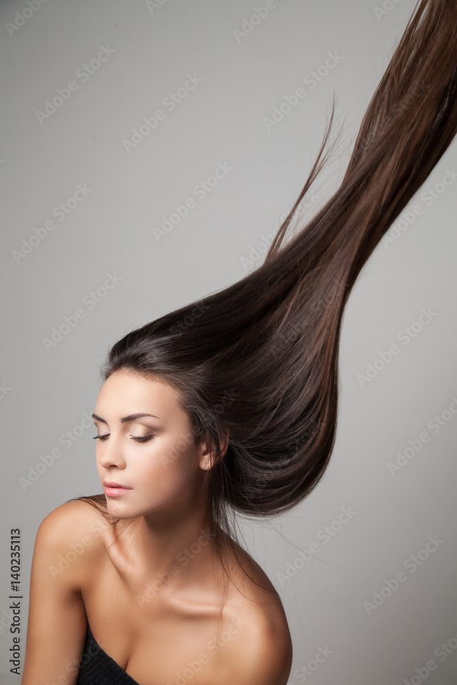 Naklejka premium Young woman posing with her long hair thrown up. Vertical studio shot.