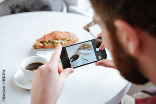 Side view of a man taking photo of his food in cafe