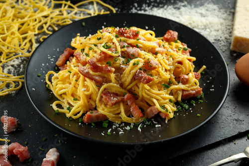 Classic Homemade Pasta carbonara Italian with Bacon, eggs, Parmesan Cheese on black plate.