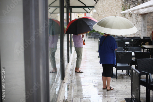 Two women with big umbrellas in the street cafe are waiting for the end of the rain.