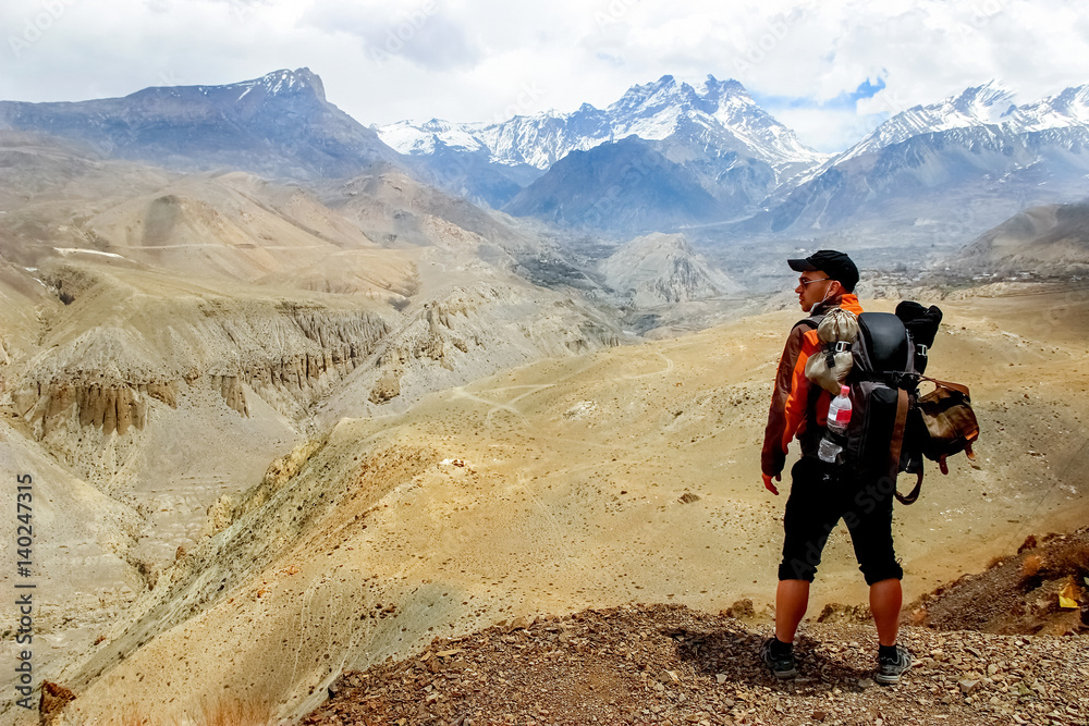 A traveler with a backpack in the Himalayan mountains looks at the gorge. Nepal. Kingdom of Upper Mustang.