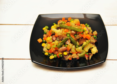 Valokuva Black plate with a vegetable saute on a white wooden background
