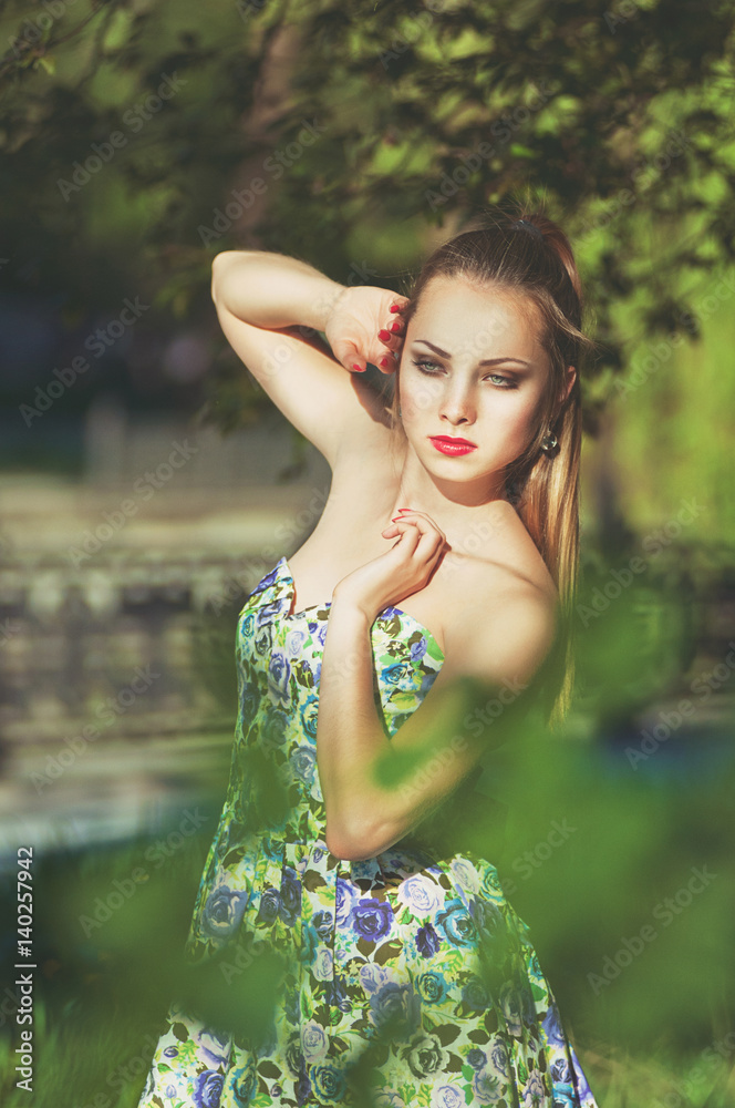 Naklejka premium Beautiful colorful toned portrait of sensual young sportive woman with emotional eyes and long hair, in floral dress, standing in park