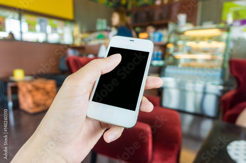 Hand holding phone in coffee shop background