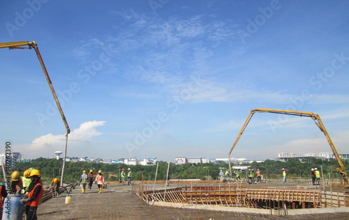 Construction workers pouring wet concrete using concrete hose from concrete pumping machine into floor slab form work at the construction site.  
