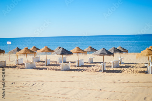 Straw umbrellas on ocean beach in Algarve Portugal, sunny outdoors background