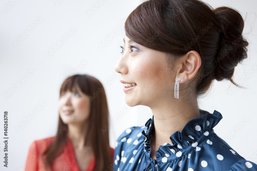 Two young women smiling and looking away, white background, differential focus