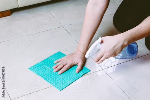 Woman with cloth and spray cleaning floor at home