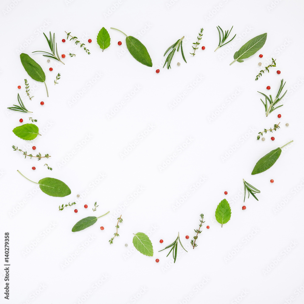 Fototapeta premium Heart shaped frame various fresh herbs rosemary, sage ,thyme and peppermint leaves flat lay with central copy space on white wooden background.