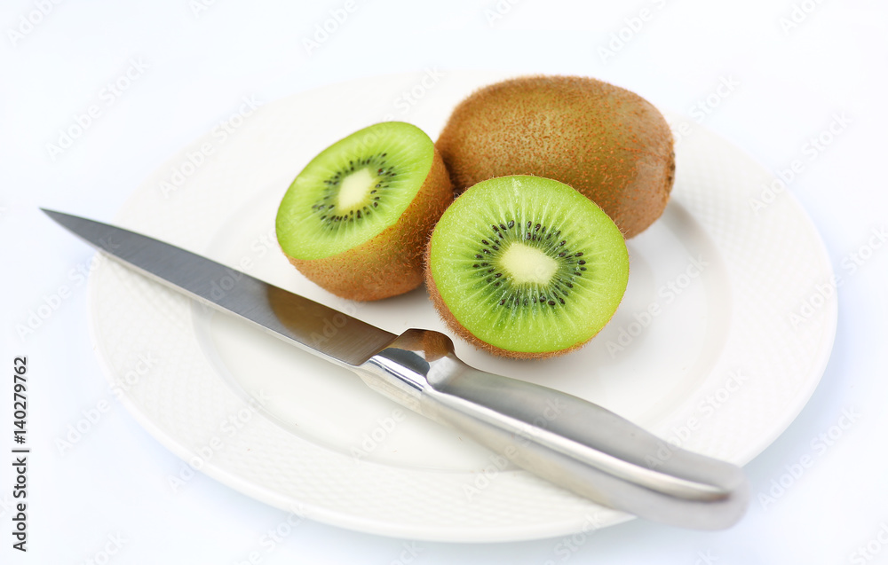 Half of juicy kiwi fruit with knife on white plate against white background Half of juicy kiwi fruit with knife on white plate against white background