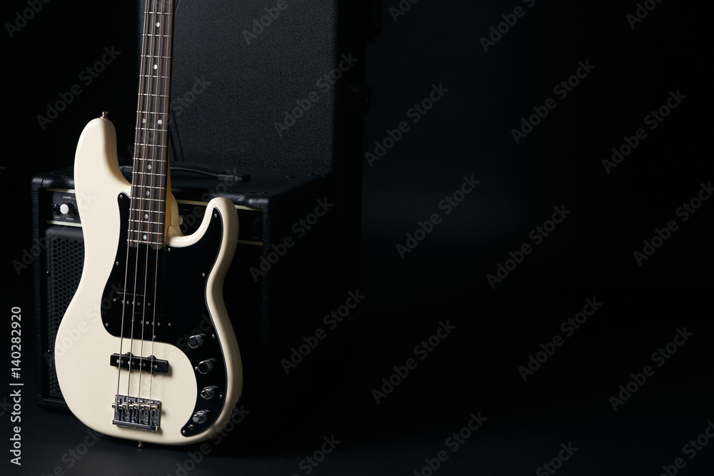 Black and white electric bass guitar with amplifier,hard case on black background with copy space.