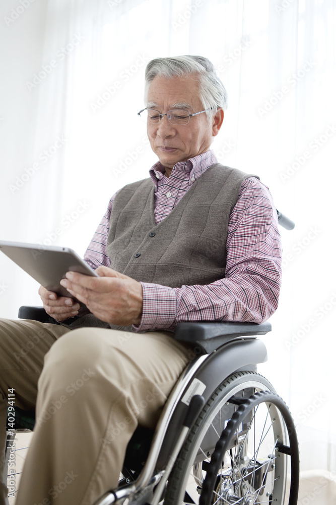 Senior man in wheelchair looking at tablet PC Senior man in wheelchair looking at tablet PC