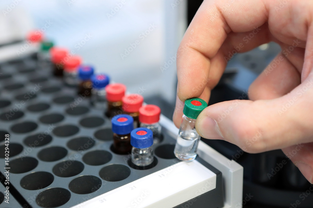 People hand holding a test tube vial sets for analysis in the gas liquid chromatograph. Laboratory assistant inserting laboratory glass bottle in a chromatograph vial