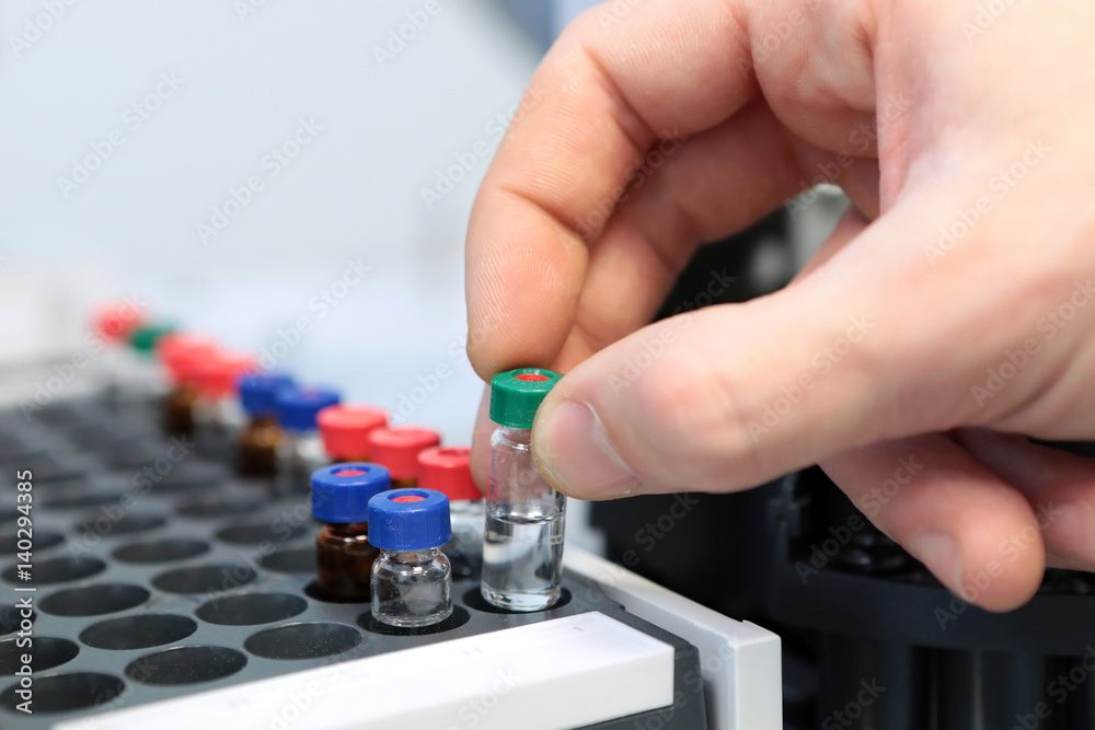 People hand holding a test tube vial sets for analysis in the gas liquid chromatograph. Laboratory assistant inserting laboratory glass bottle in a chromatograph vial People hand holding a test tube vial sets for analysis in the gas liquid chromatograph. Laboratory assistant inserting laboratory glass bottle in a chromatograph vial