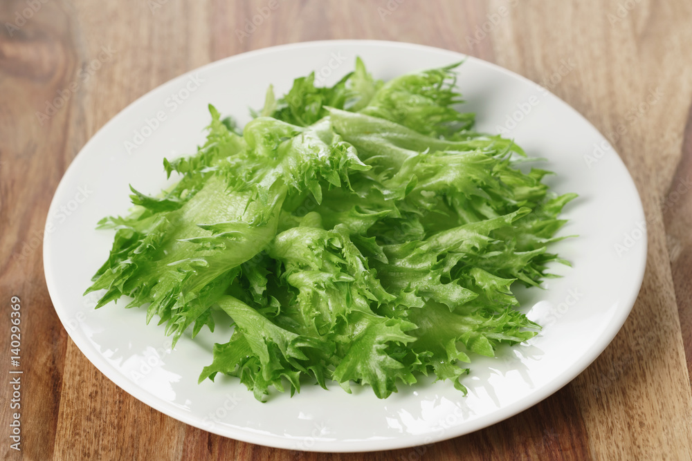 green frillies lettuce on white plate on wooden table, closeup photo