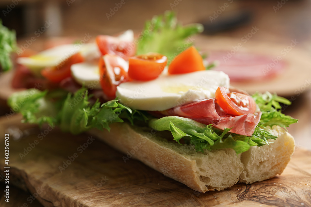 open sandwich with prosciutto, mozzarella and tomatoes on kitchen table, shallow focus open sandwich with prosciutto, mozzarella and tomatoes on kitchen table, shallow focus