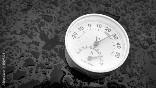 Analog hygrometer putting on a black background filled with drop of water after rain.