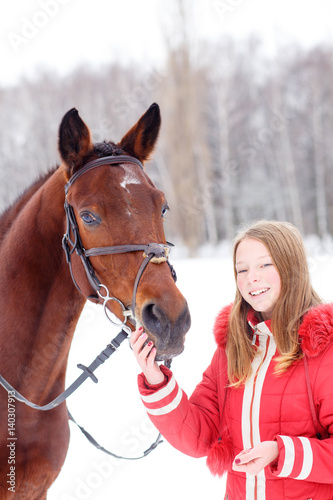 Young teenage girl spending time with her friend bay horse in winter park. Friendship concept image