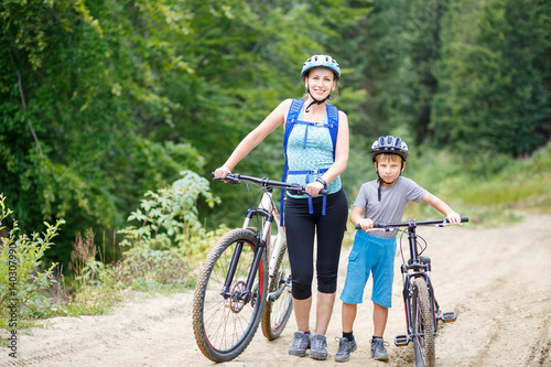Young woman with her son standing with bikes in mountain forest