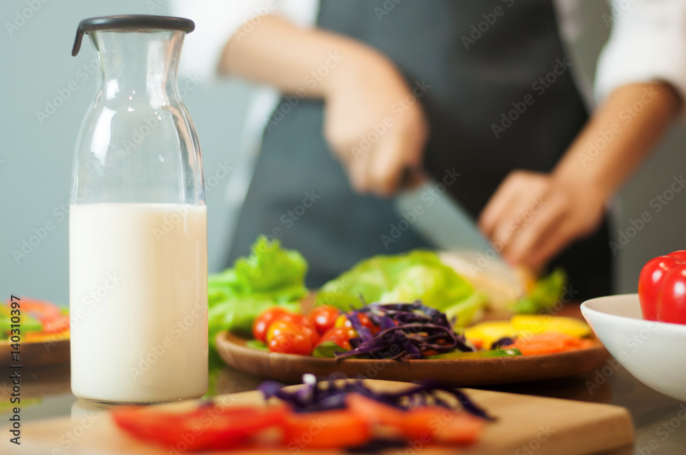 Milk in bottle with woman cooking and vegetables.