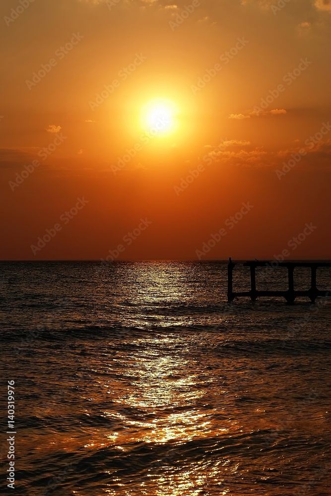 Golden natural sea sunset view of small bridge at horizon and red sky landscape. Sunset reflection in nature with sun in clouds. Golden natural sea sunset view of small bridge at horizon and red sky landscape. Sunset reflection in nature with sun in clouds.