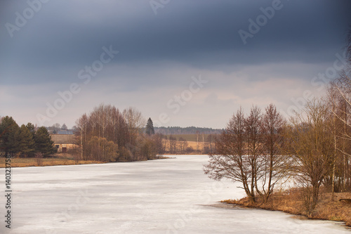 Spring rural scene. Lake under ice and snow melting. Cloudy spring day