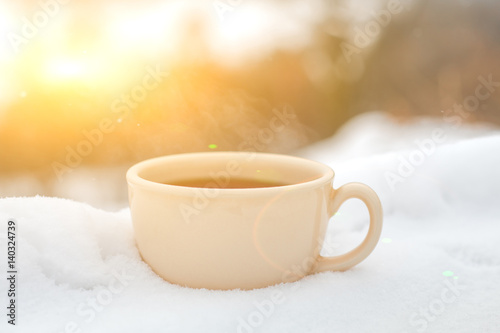 Nice warm cup of tea or coffee outdoors on the snow on a background of a winter landscape. Cozy winter still life.