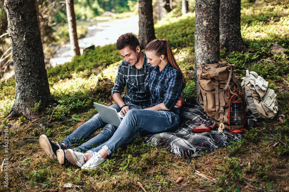 A couple of tourists sitting and looking at laptop in the woods. The concept of active rest A couple of tourists sitting and looking at laptop in the woods. The concept of active rest