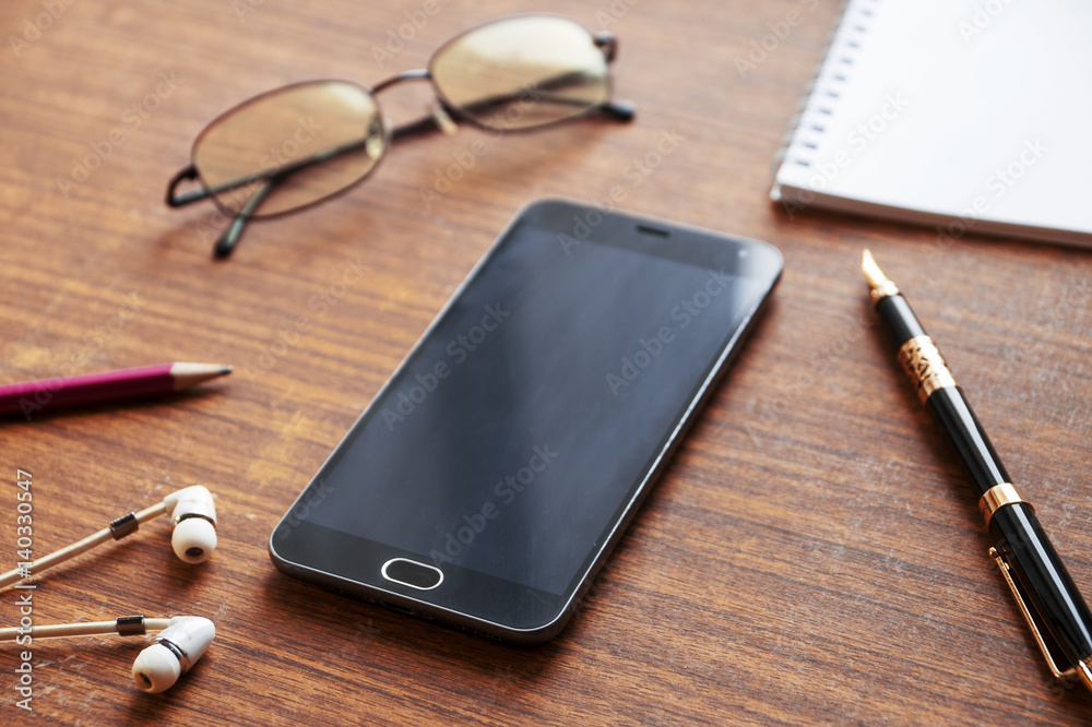 View of business have a phone, notebook, Goggles, headphones, pen and mobile phone with on wooden red background View of business have a phone, notebook, Goggles, headphones, pen and mobile phone with on wooden red background